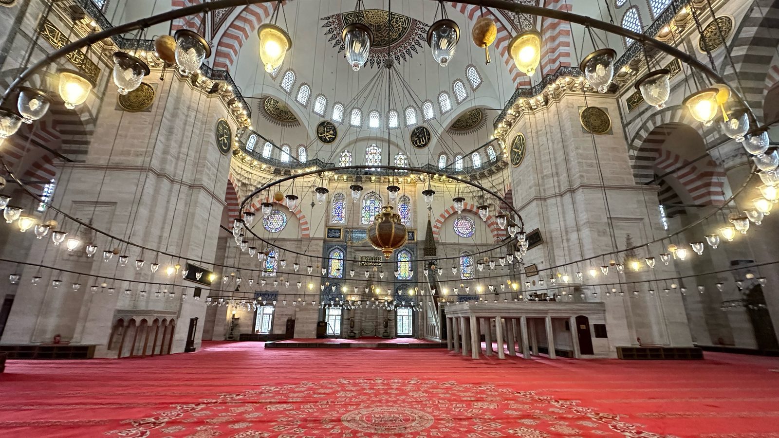 The Süleymaniye prayer hall with its red patterned carpet, large ring chandelier and dome overhead.