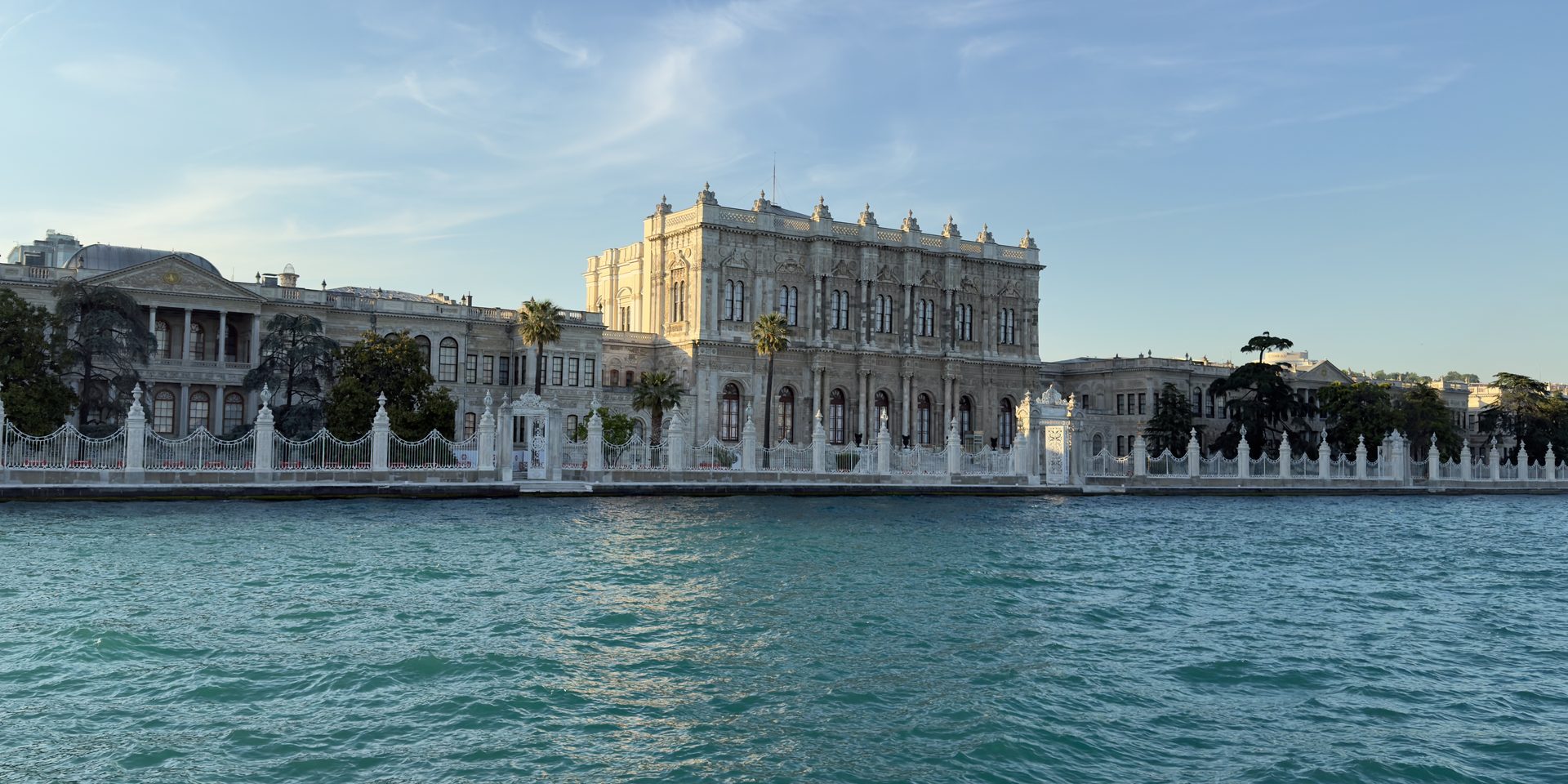 Dolmabahçe Palace's pale stone facade with arched windows seen from the Bosphorus at early evening
