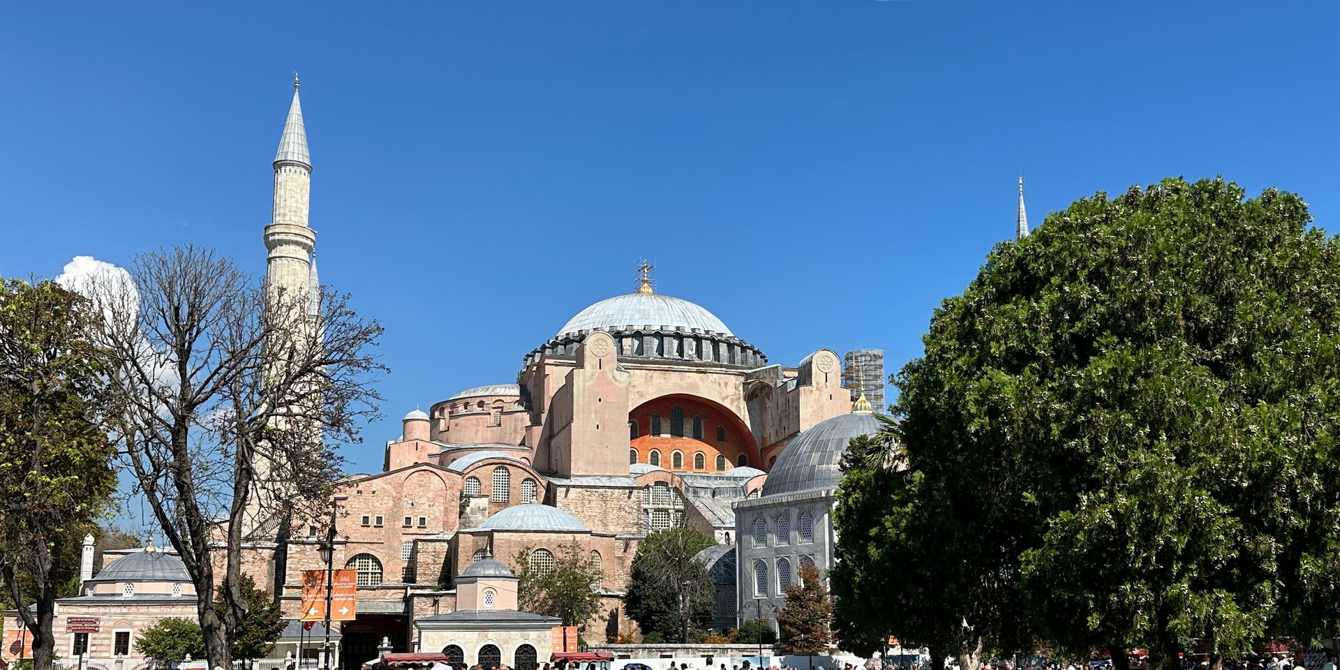Hagia Sophia seen from Sultanahmet Park: grey central dome, pinkish-red facade, one white minaret and clear blue sky