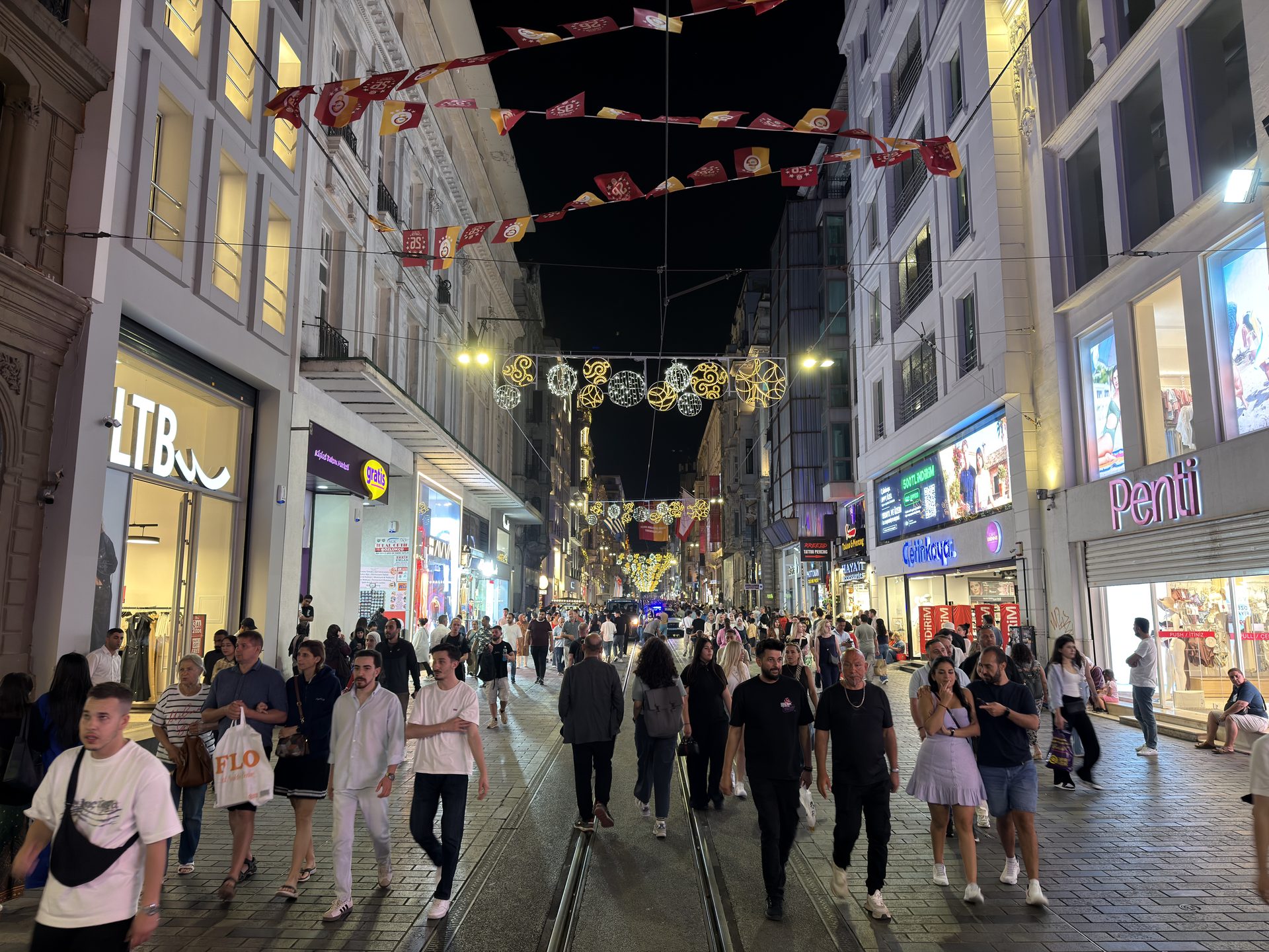 Evening shopping crowd on Istiklal Street, storefronts lit under festive banners