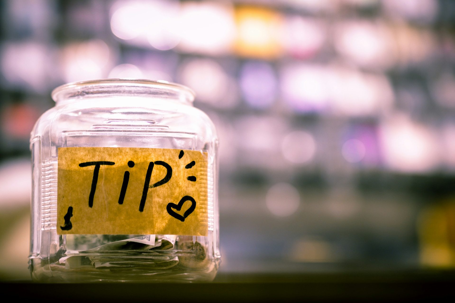 A glass tip jar with a few notes and coins on a counter