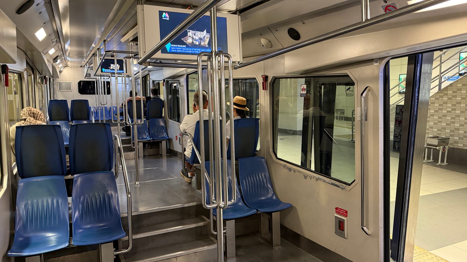 Interior of an F1 funicular car with stepped floor levels, blue seats and steel grab poles.