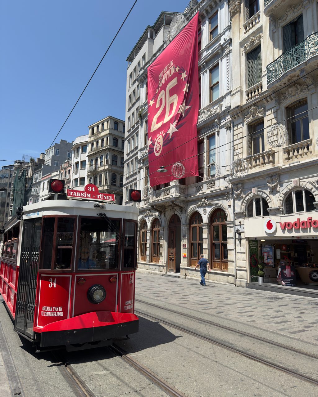 Red-and-cream heritage tram on street tracks along İstiklal, passing ornate 19th-century facades.