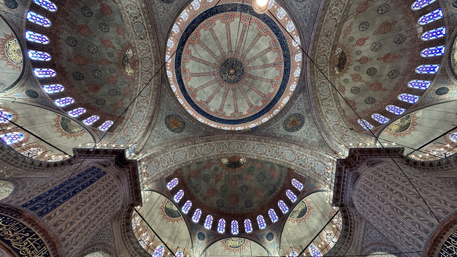 Looking straight up into the Blue Mosque central dome and semi-domes, with painted patterns and rows of small arched windows.