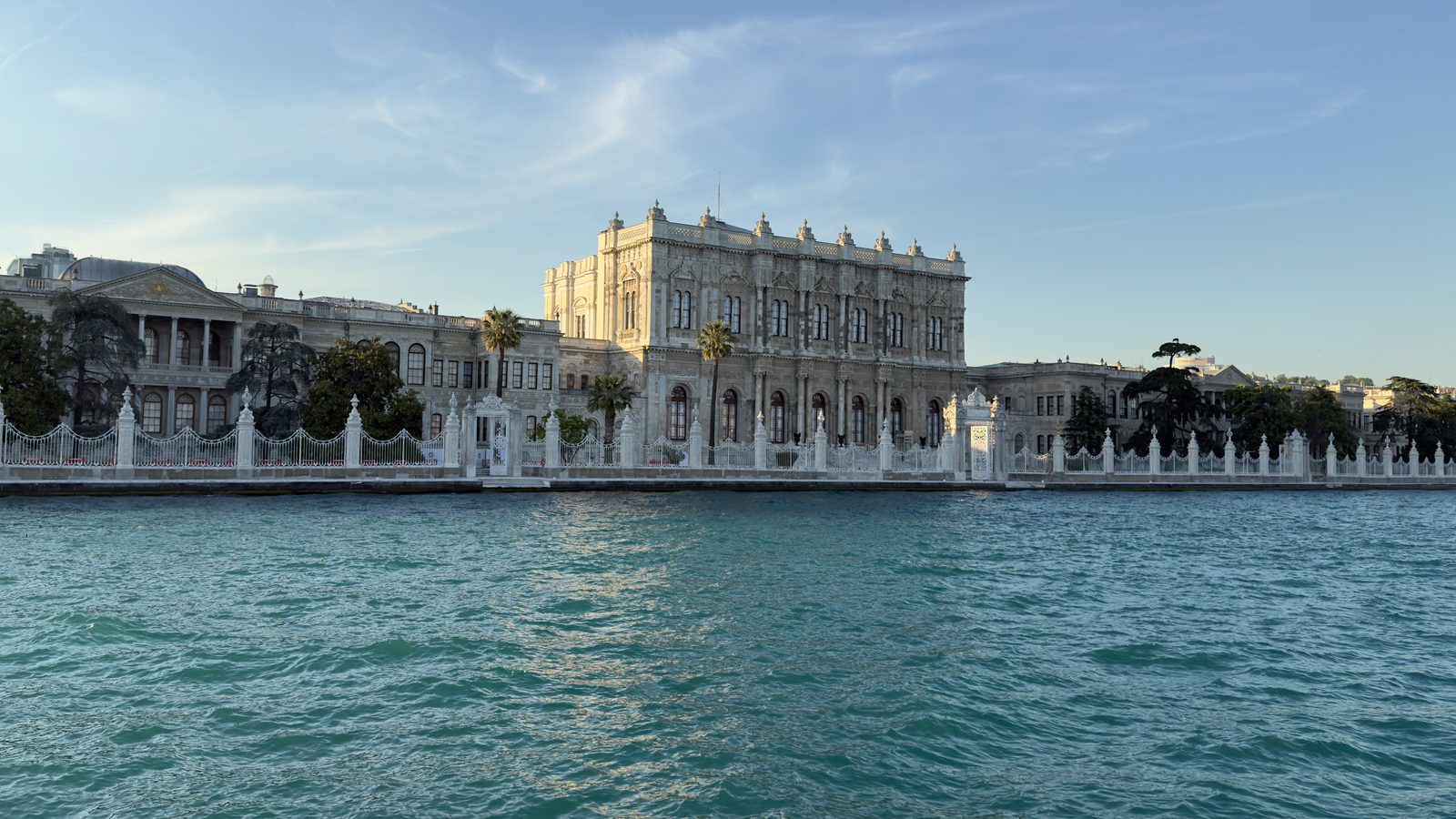 Dolmabahçe Palace's pale stone facade with arched windows seen from the Bosphorus at early evening