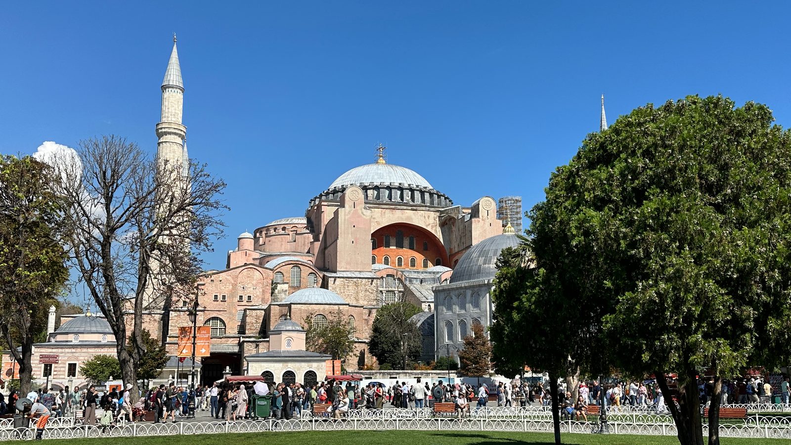 Hagia Sophia seen from Sultanahmet Park, central dome and red arched facade framed by trees, visitors on the path below
