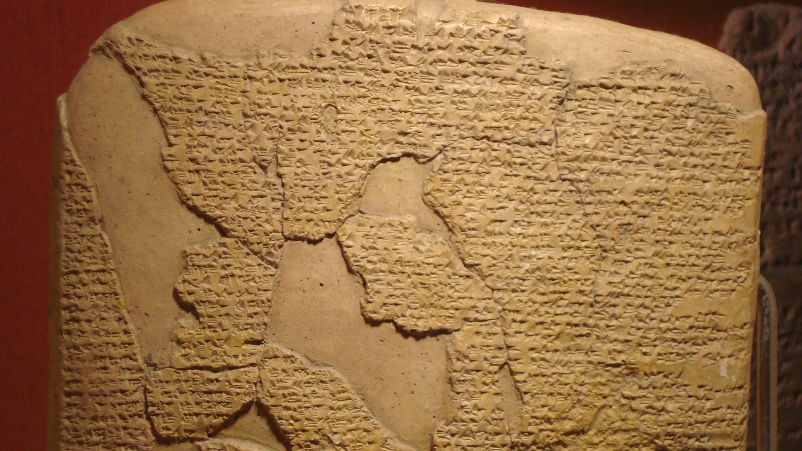 Close-up of the Kadesh treaty clay tablet, its surface covered in cuneiform script against a red backdrop.